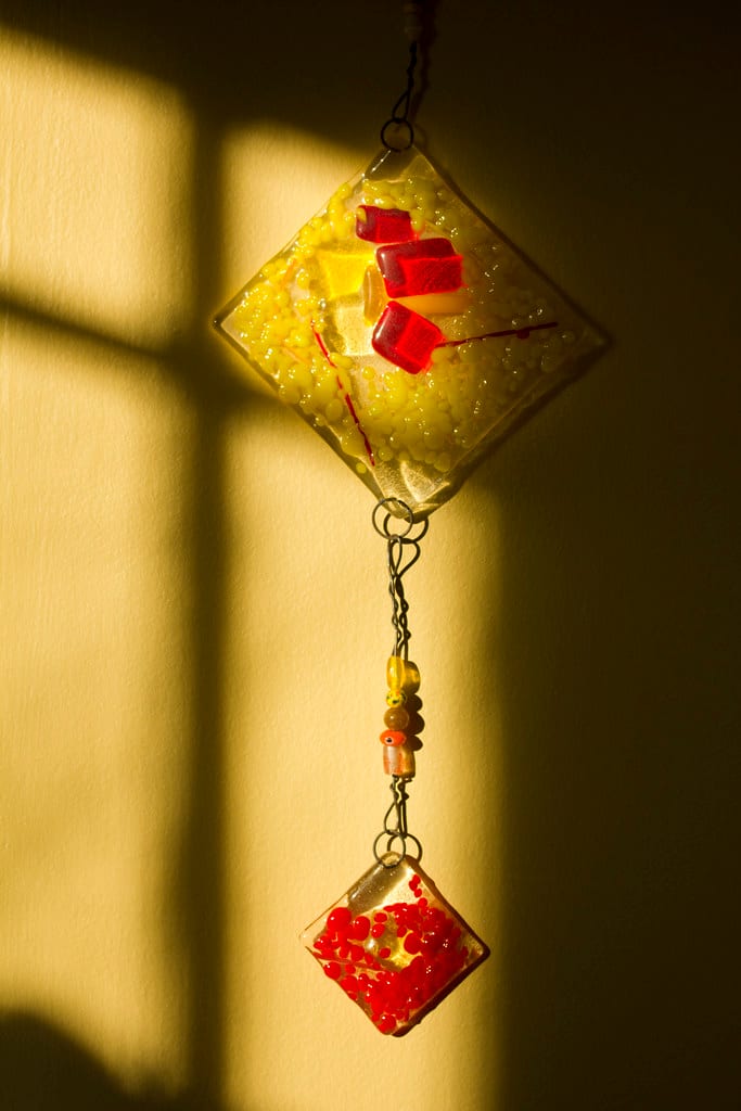 Multiple kiln-formed glass pieces in blues, greens, and clear hanging in a display: bowls, pendants, and flat panels showing the range of work a glass fusing kiln produces
