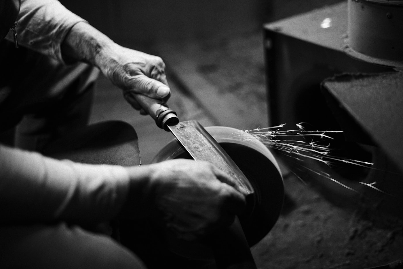 Hands holding a blade against a grinding wheel, sparks streaming off the edge