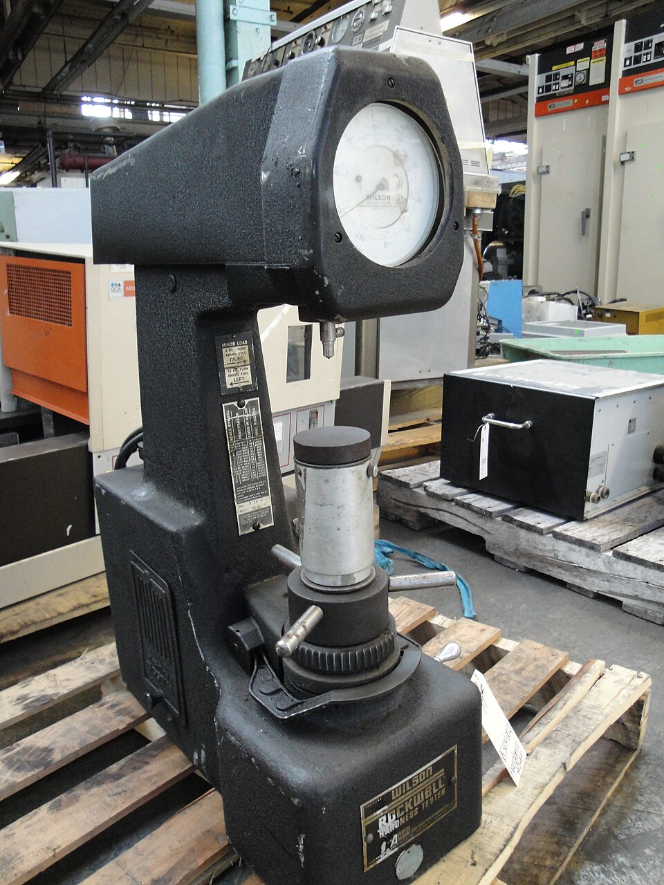 A benchtop Rockwell hardness tester with the indenter above a steel anvil