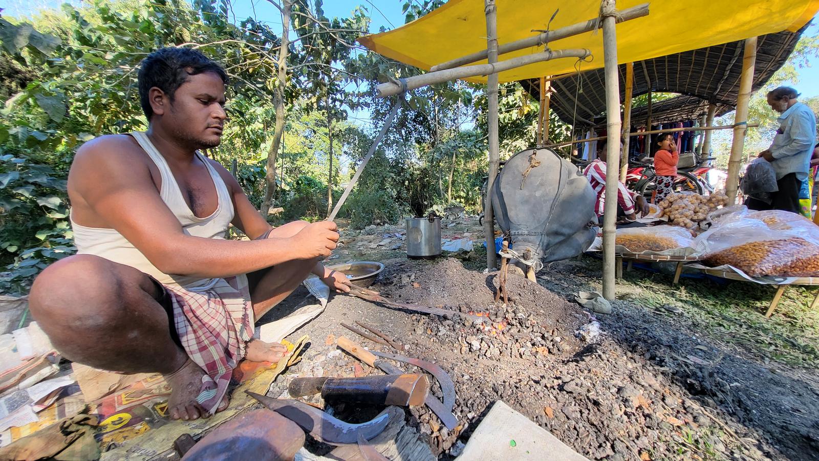 A bladesmith working on knives at an open-air workshop in a market