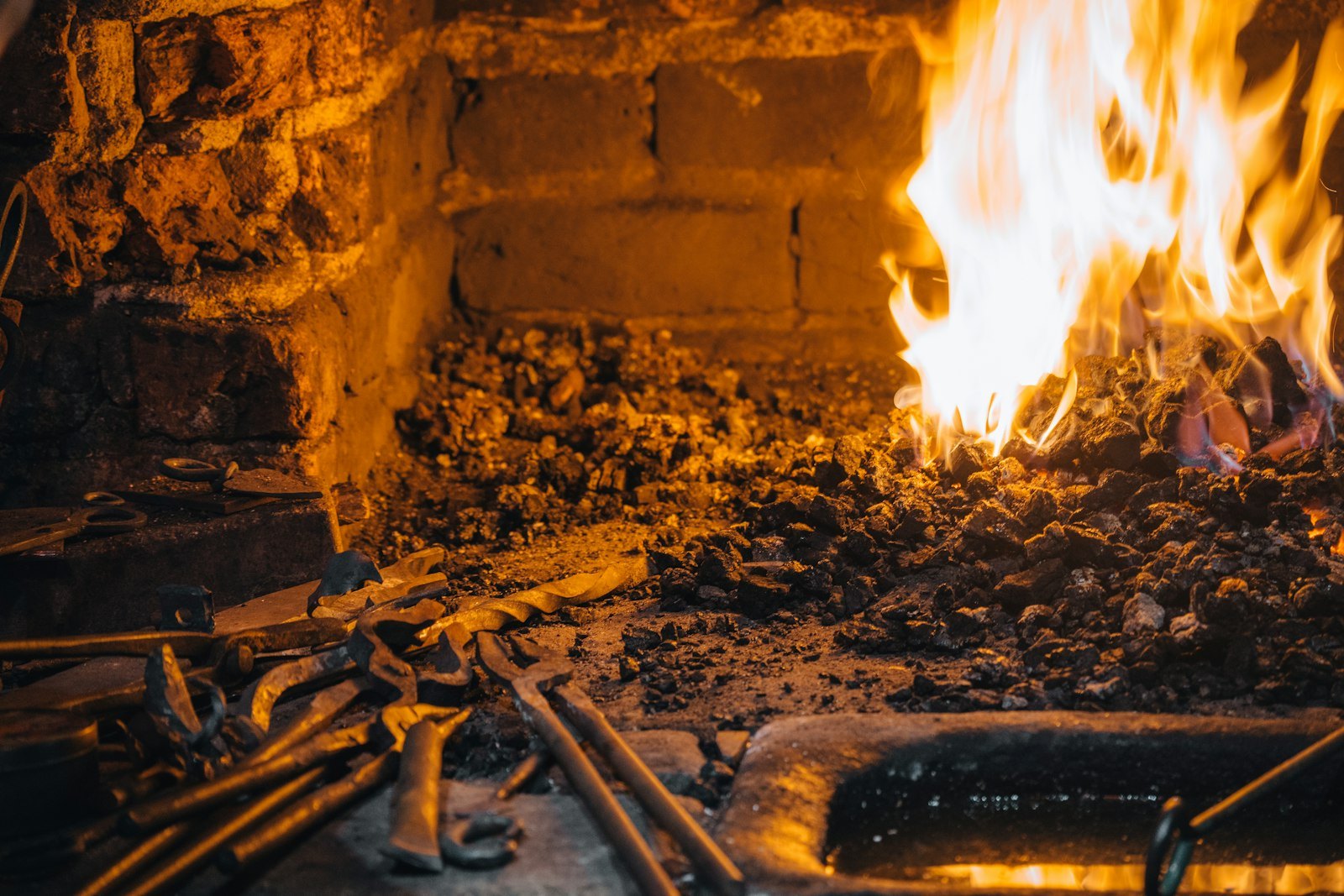 A coal forge burning with tools laid across the front of the firepot