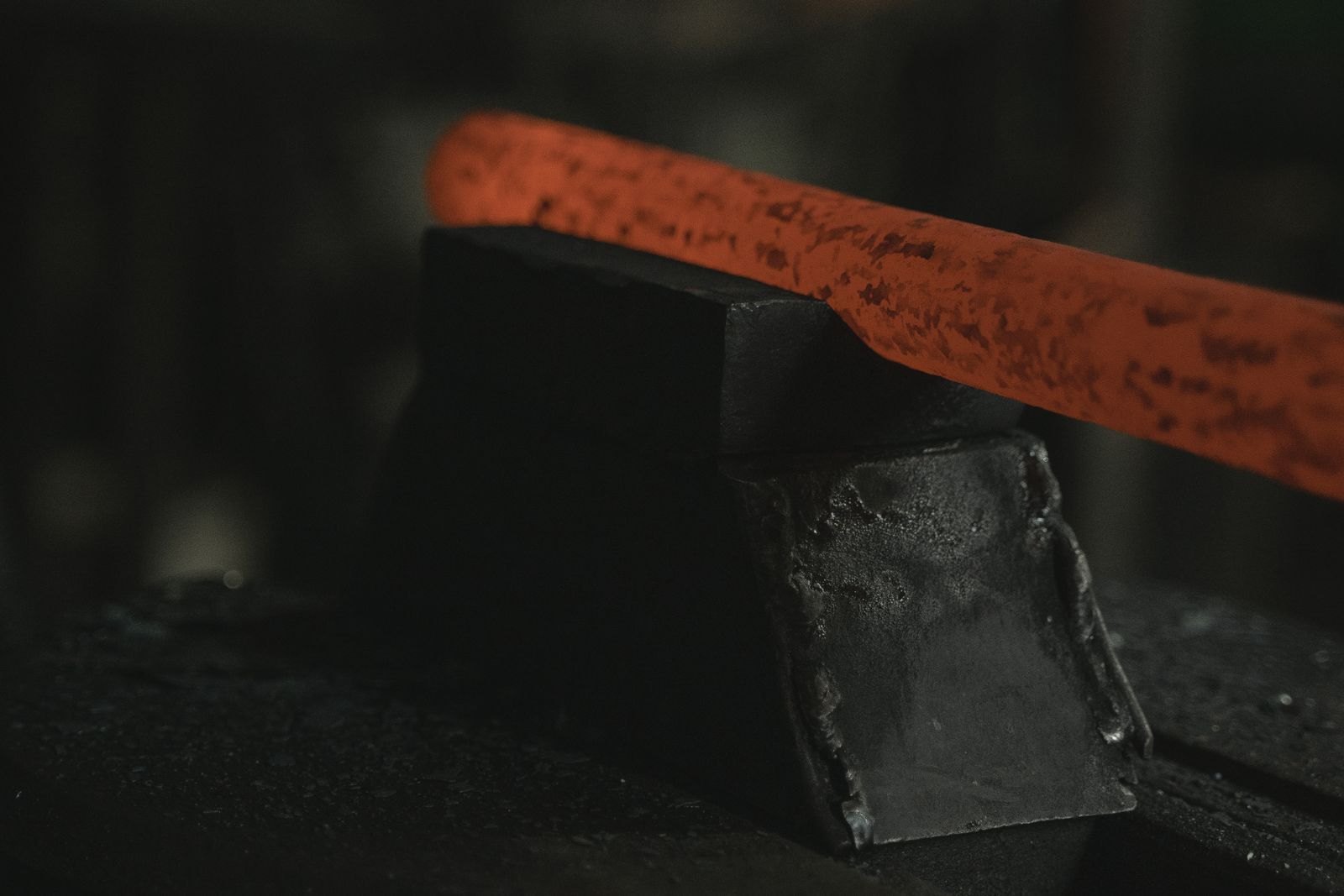 A bar of steel glowing orange at forging heat resting on a dark anvil