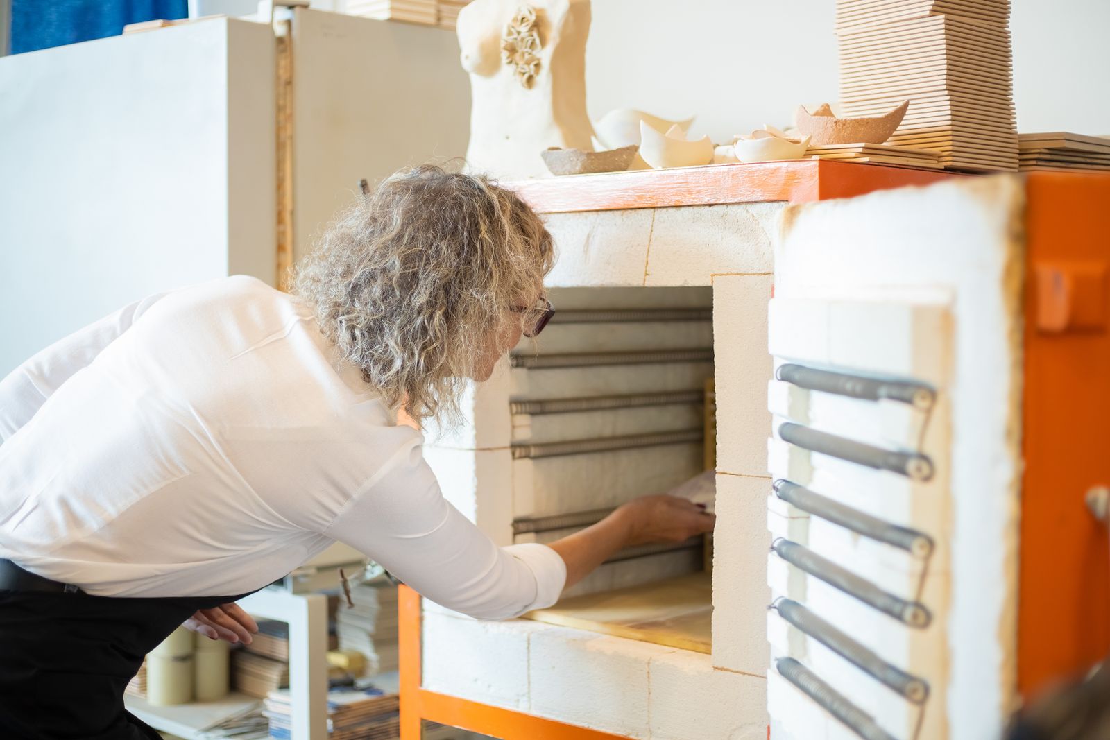 Potter loading ceramic pieces into a top-loading electric kiln for bisque firing