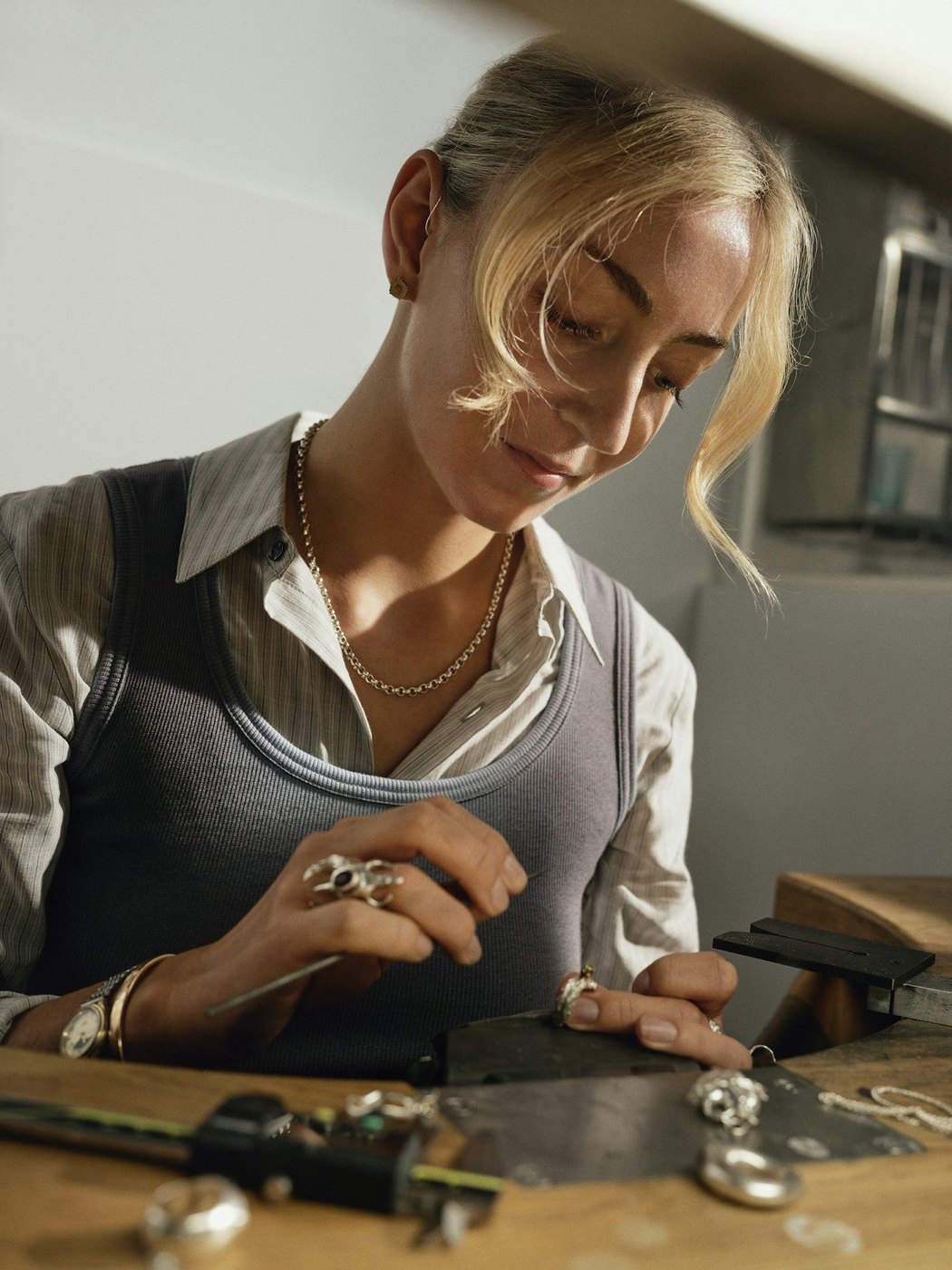 A jeweller working at a bench with small tools and finished pieces laid out