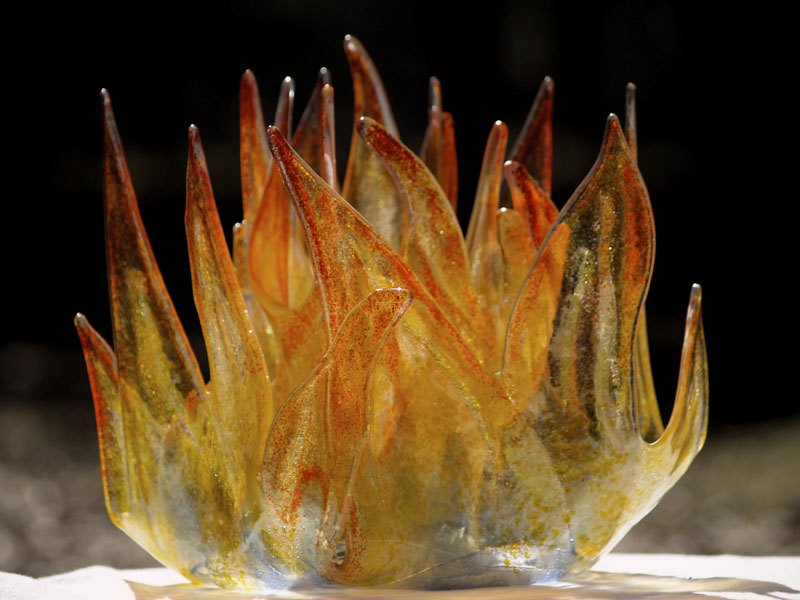 A fused and kiln-formed glass sculpture with tall amber and orange flame-shaped points