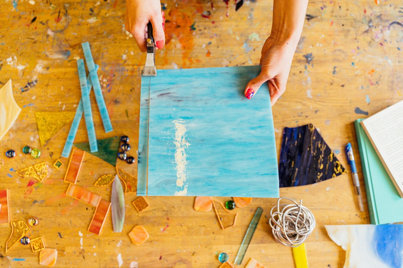 Hands arranging cut sheets of coloured glass on a wooden workbench