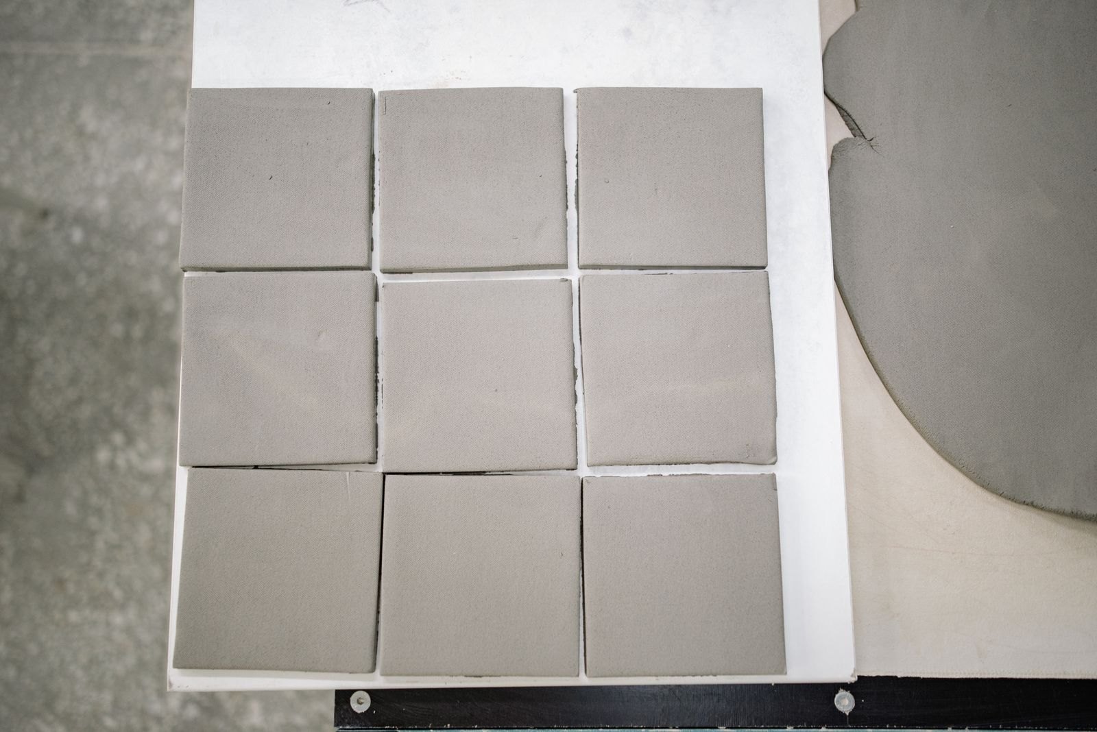 Nine square clay test tiles cut and laid out on a board in a studio