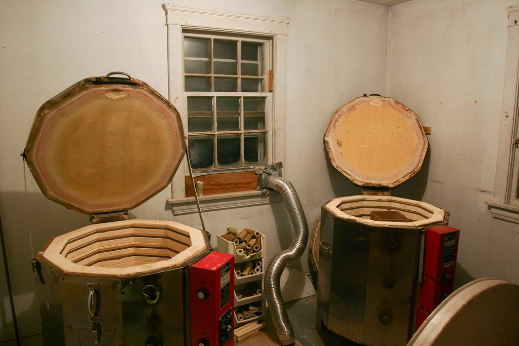 Two electric top-loading kilns standing side by side in a studio, lids open