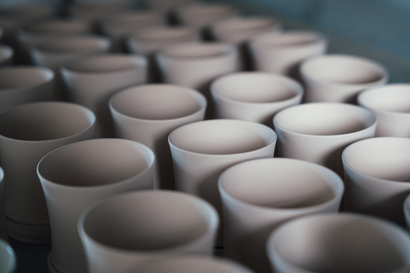 Rows of unglazed ceramic cups standing close together on a workshop rack