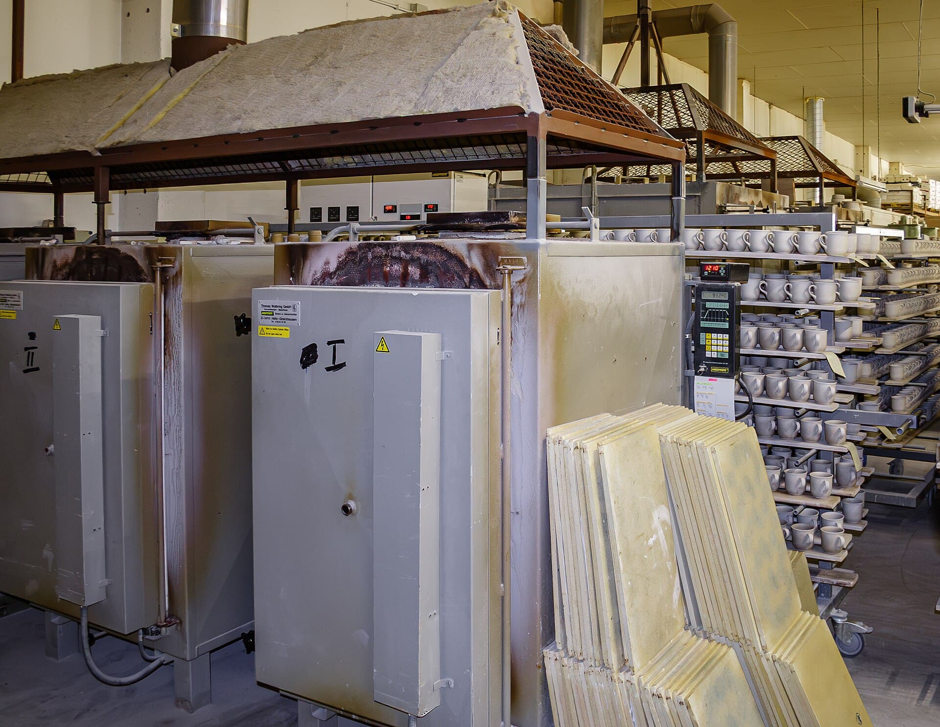 A row of large production kilns beside racks of unfired ware in a ceramics works