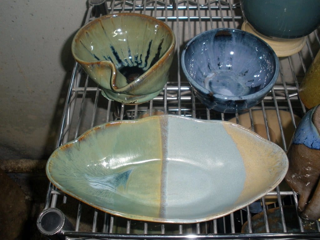 Small glazed pots and bowls cooling on a wire rack after firing
