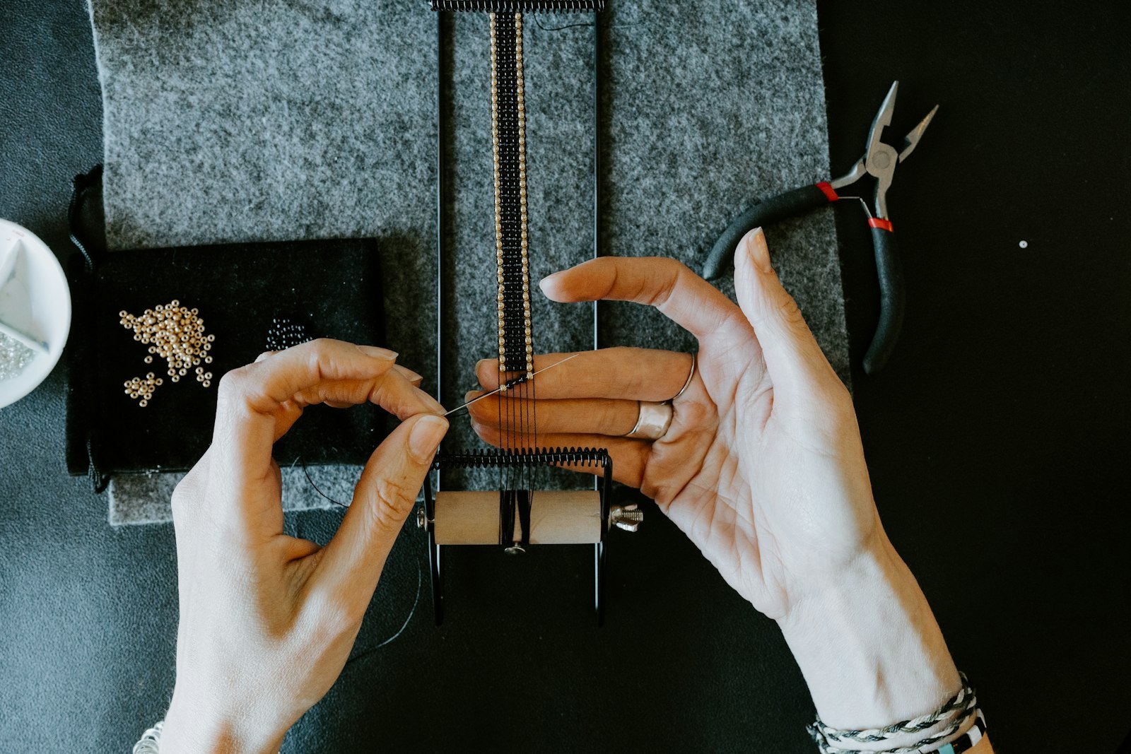 Hands using pliers on a small metal component over a felt bench mat