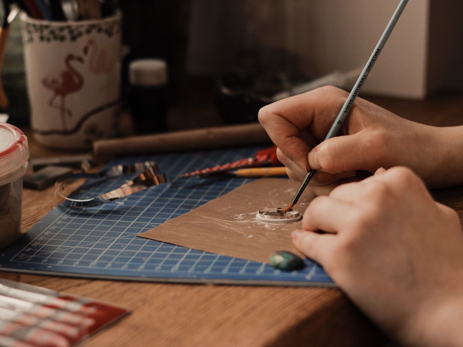 Hands working a small piece with a fine tool on a green cutting mat