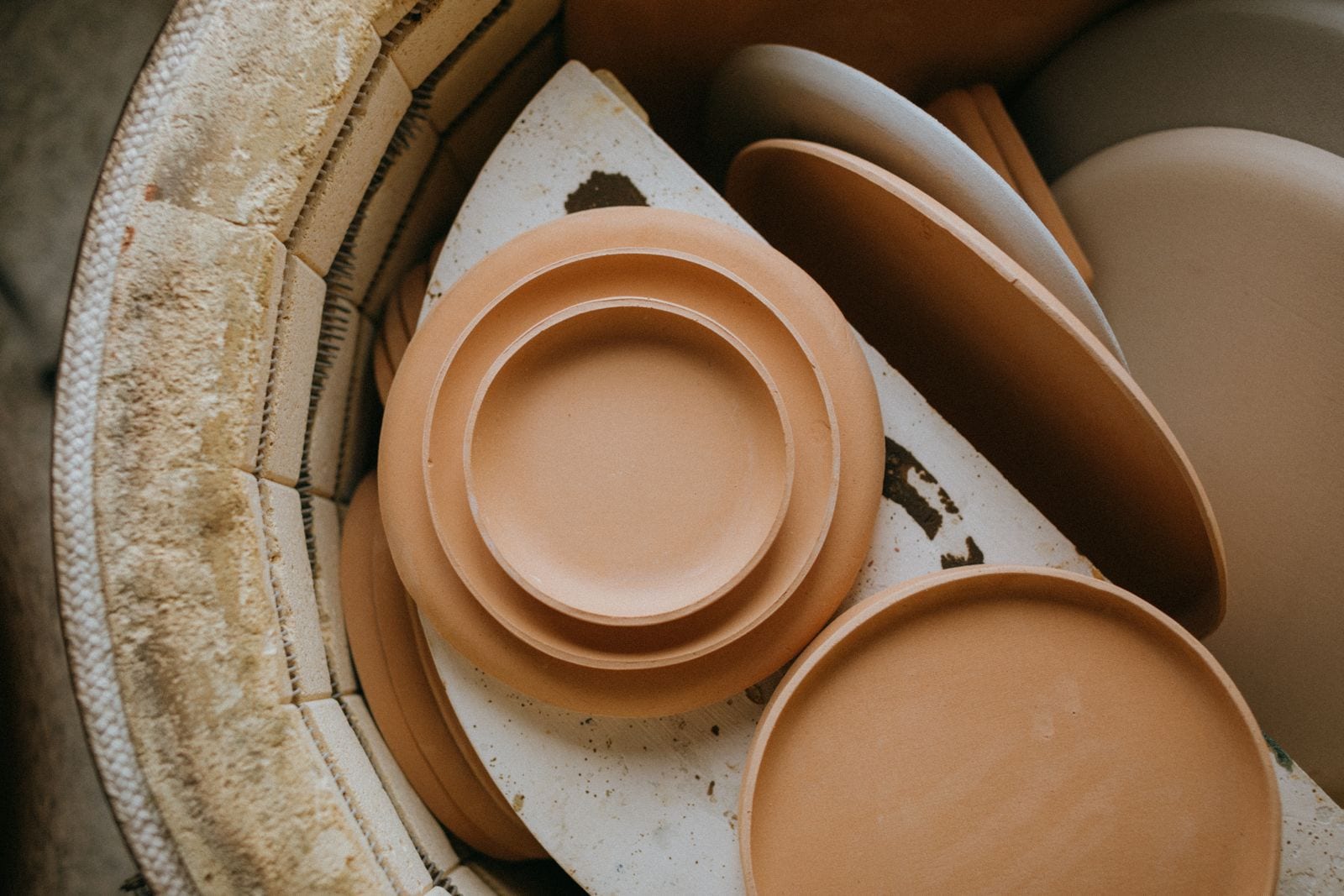 Stacked ceramic plates inside a kiln with the firebrick chamber wall behind them