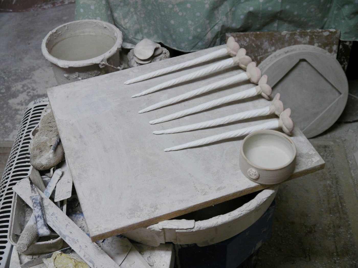 Clay tools and trimmed pottery pieces drying on a dusty wooden work board