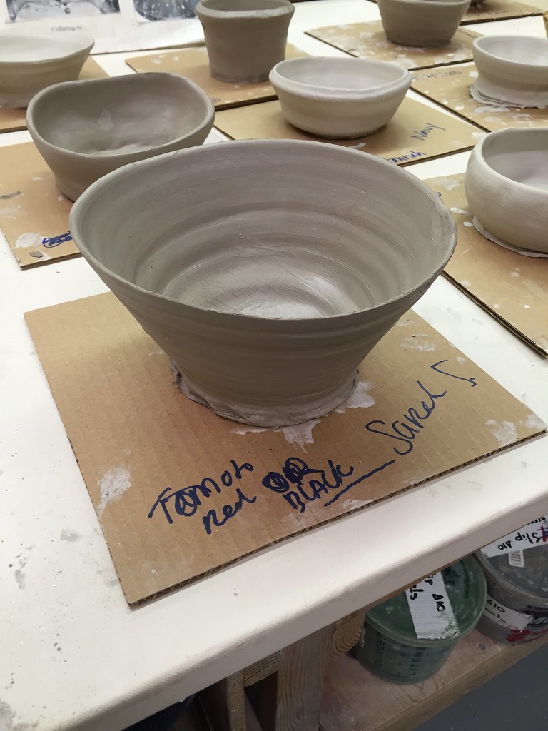 Beginning potter pulling walls of a clay cylinder on a pottery wheel