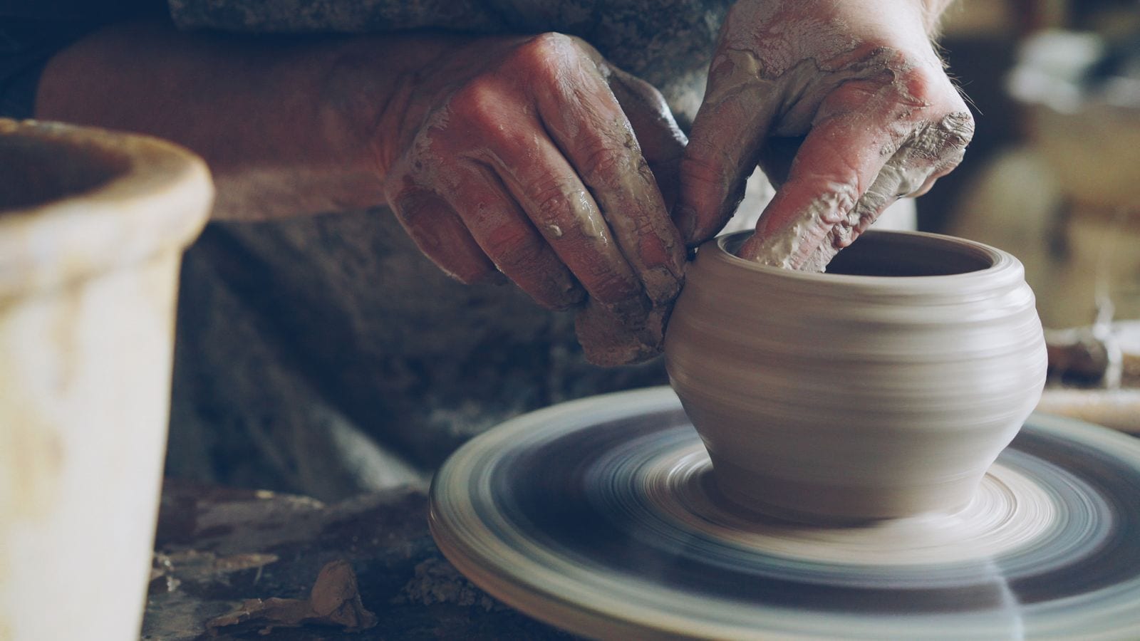 Potter's hands shaping a clay pot on a spinning wheel head
