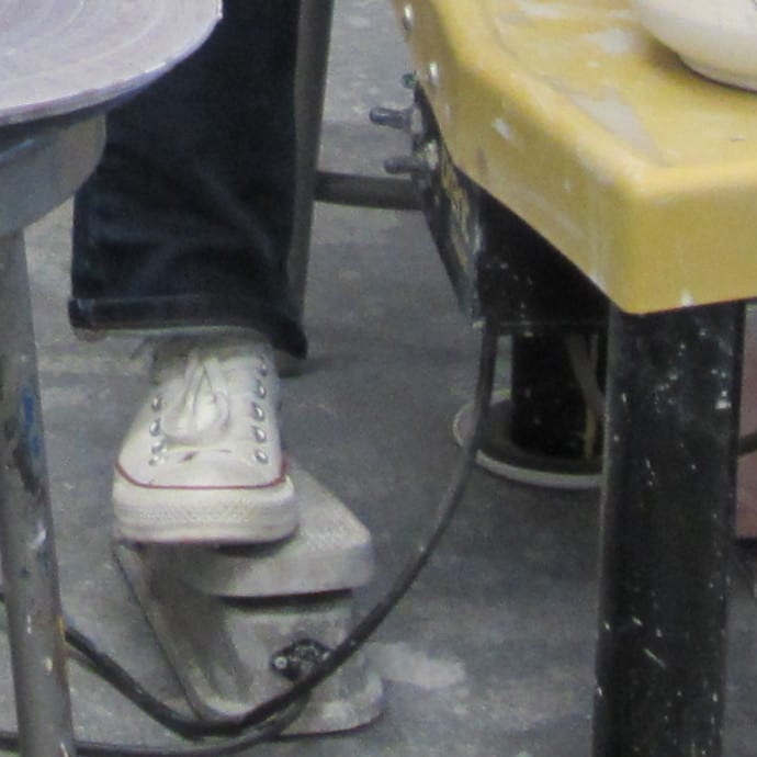 Foot pedal beneath a pottery wheel with a potter's foot resting on it during use