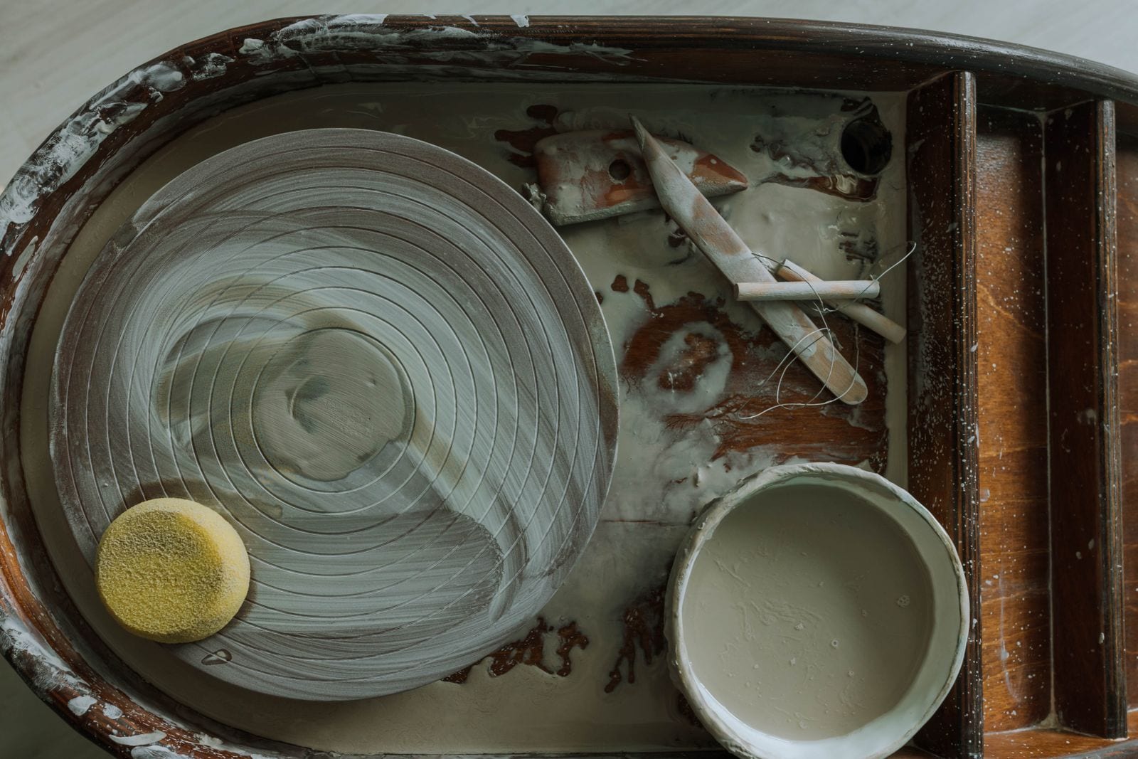 Overhead view of a pottery wheel head, splash pan and hand tools in a working studio