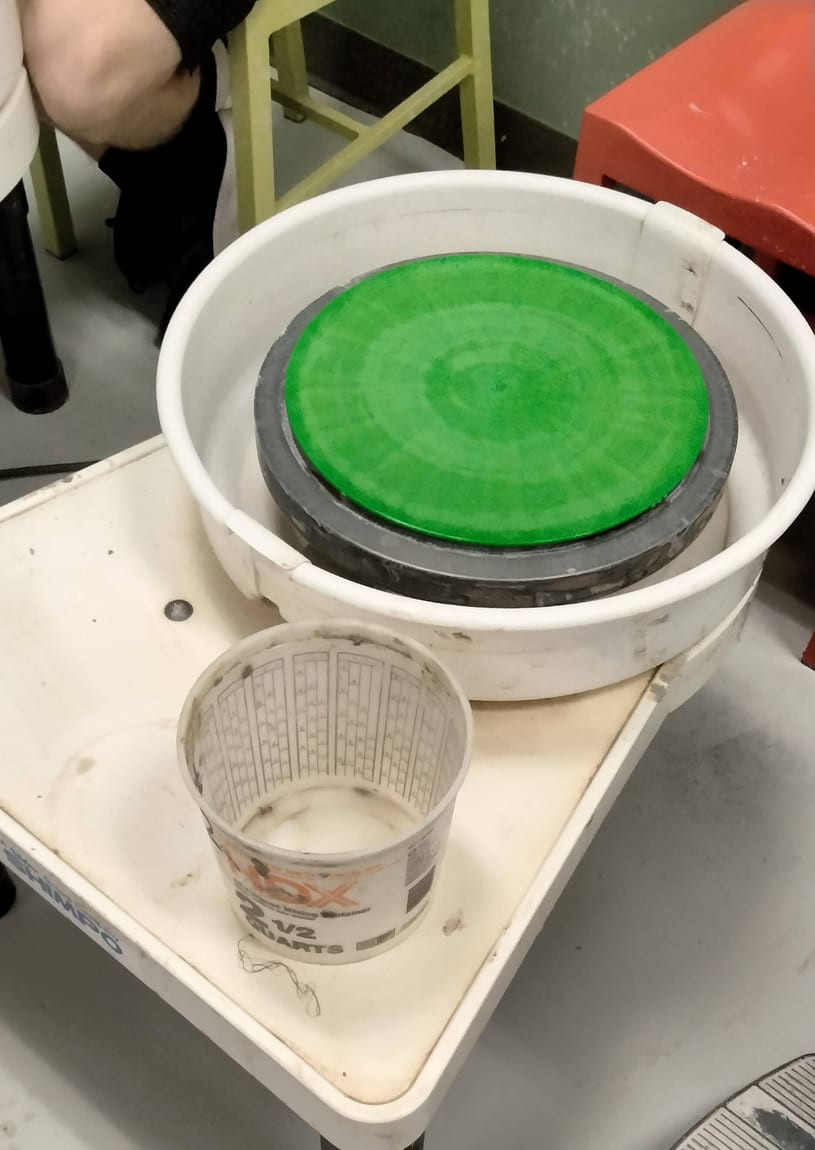 Close-up of an electric potter's wheel head seated in its pan with a bowl beside it